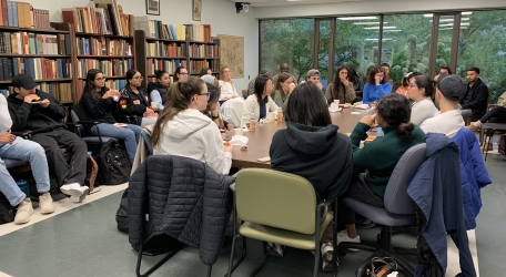 A group of students sitting around a central table. bookshelves line the room